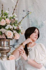 woman wearing lots of jewelry next to a bouquet of flowers