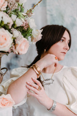 woman wearing lots of jewelry next to a bouquet of flowers