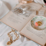 a ring sits in a ring dish atop an open book, a bracelet sits in front of it