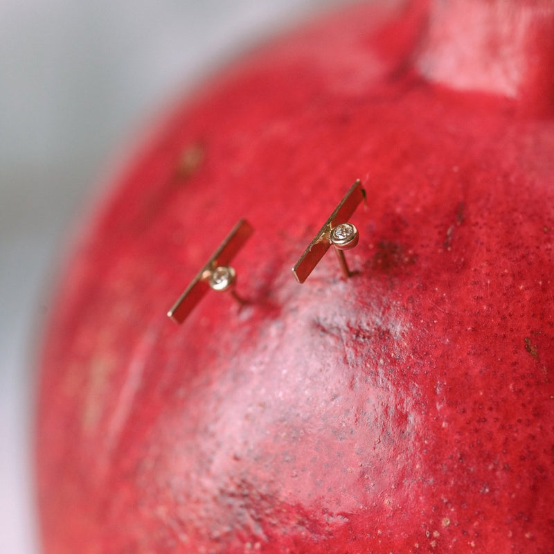 two gold and diamond post earrings in the side of a pomegranate