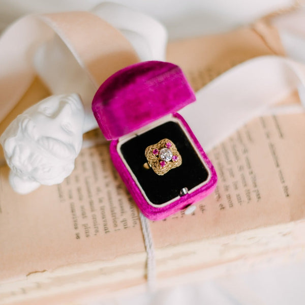 gold ring with a center diamond and four rubies sitting in a ring box